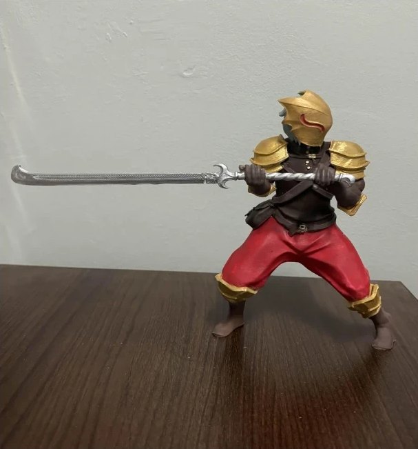 The finished 3D print on a wooden table: the Ironclad in a wide stance, holding a long glaive, painted with a gold helmet and pauldrons and red trousers